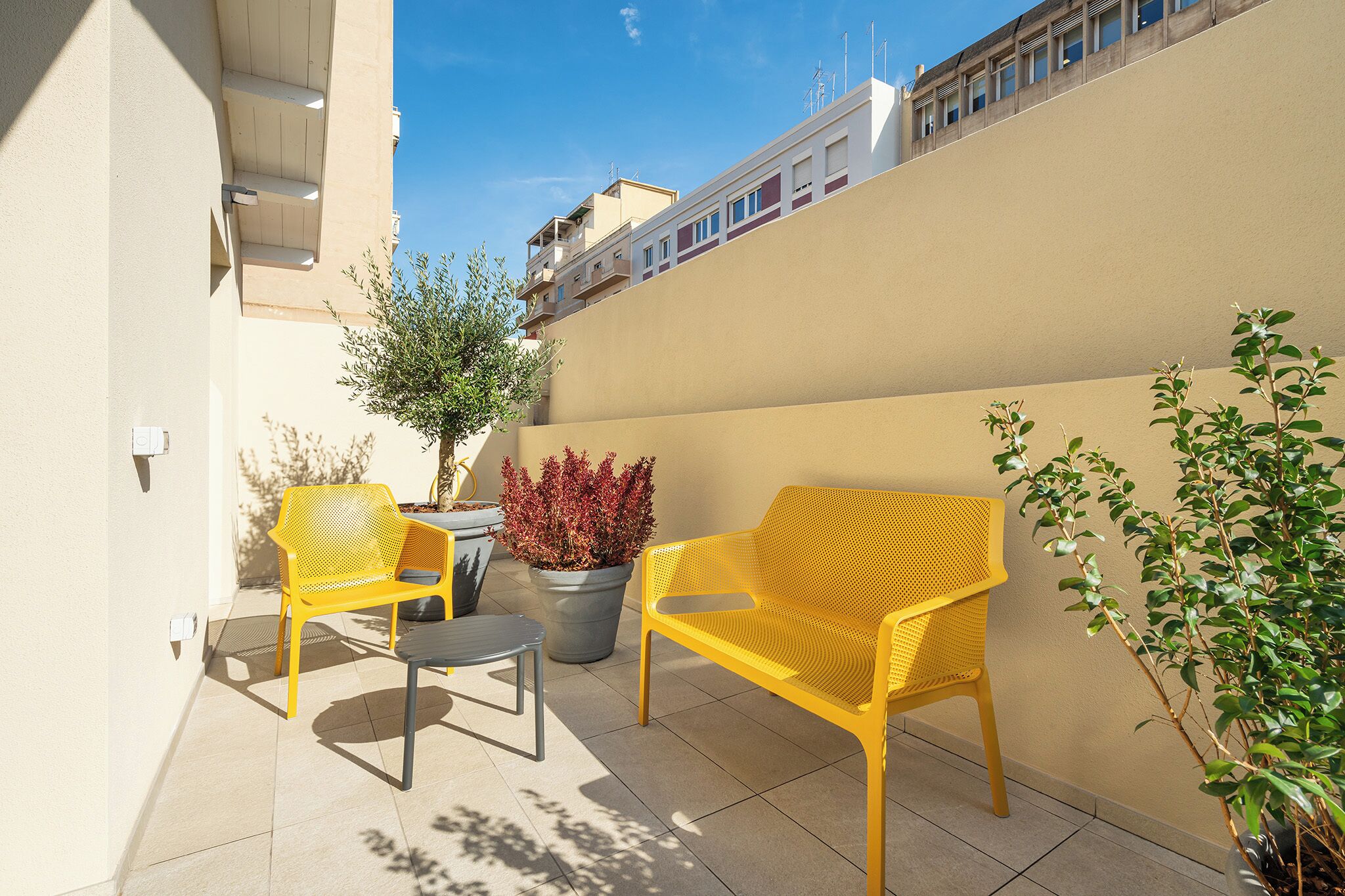 A small outdoor patio with two yellow chairs, a table, and potted plants.