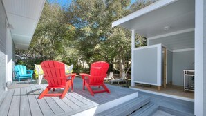 Une terrasse en bois avec des fauteuils Adirondack rouges, une petite table et un bâtiment blanc doté d’une zone abritée.