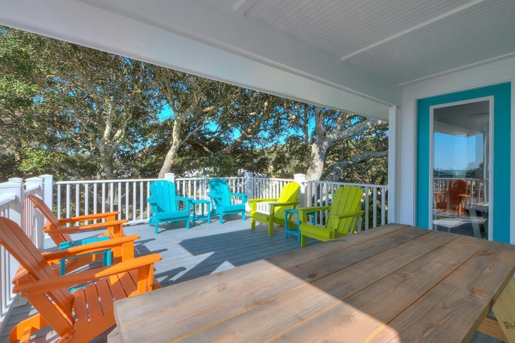 A covered outdoor deck with colorful Adirondack chairs and a wooden table.