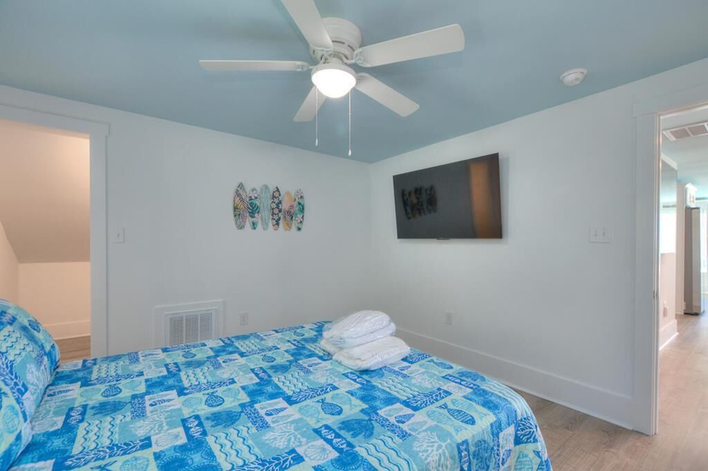 A bedroom with a bed, a ceiling fan, a TV, and wall art.