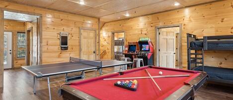 Une pièce en bois équipée de tables de ping-pong, d’une table de billard et d’une table de jeu de flipper.
