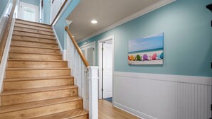 Una escalera de madera con barandillas blancas que lleva a una habitación con paredes color turquesa y un cuadro con motivos playeros.