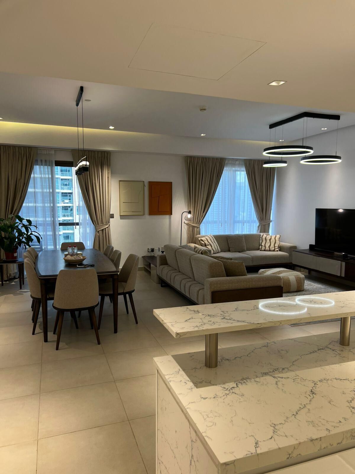 A modern living room with a dining area, a sofa set, a TV, and a marble coffee table.