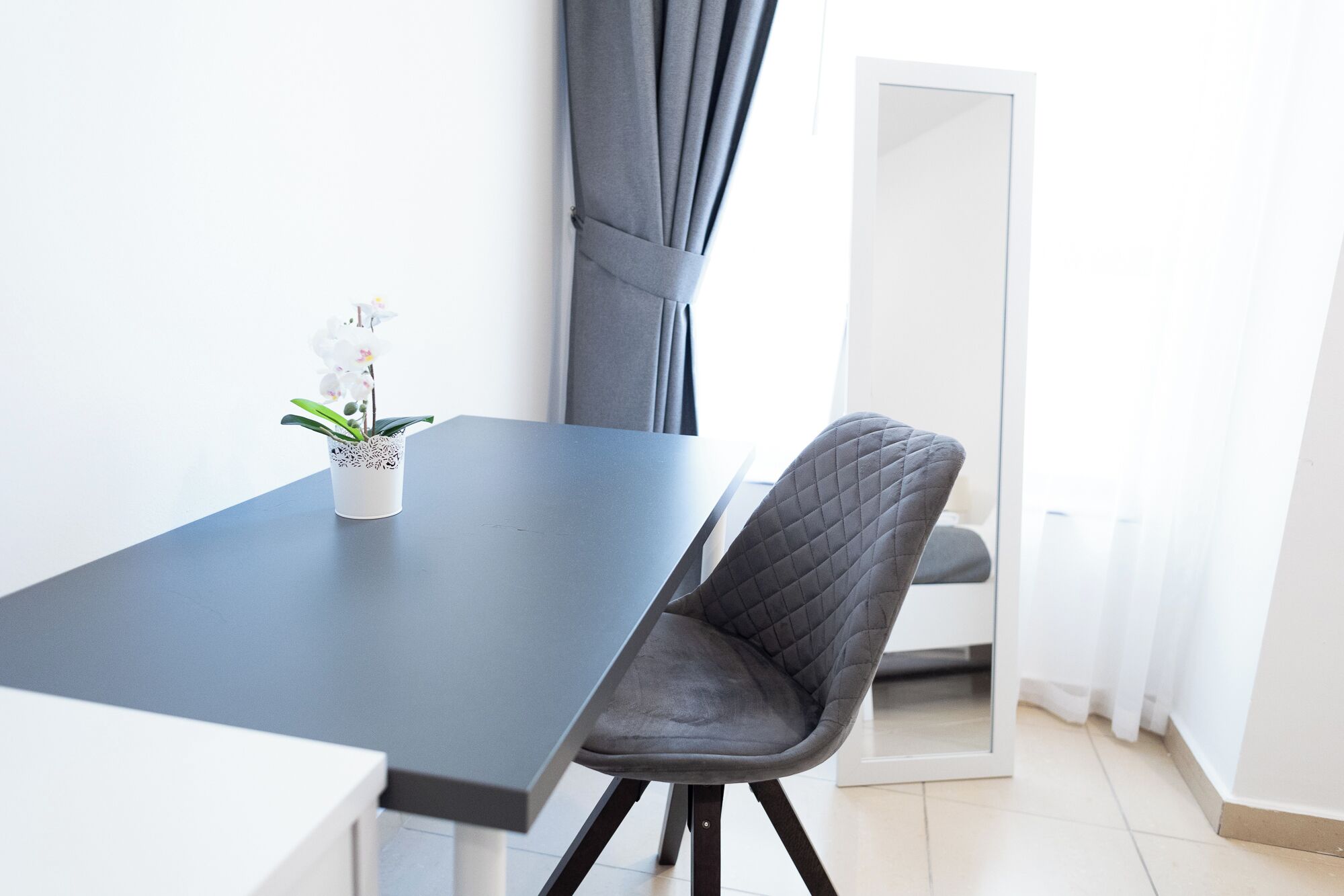 Une pièce moderne avec une table de couleur gris foncé et une seule chaise grise. On peut voir un vase blanc avec une plante sur la table.