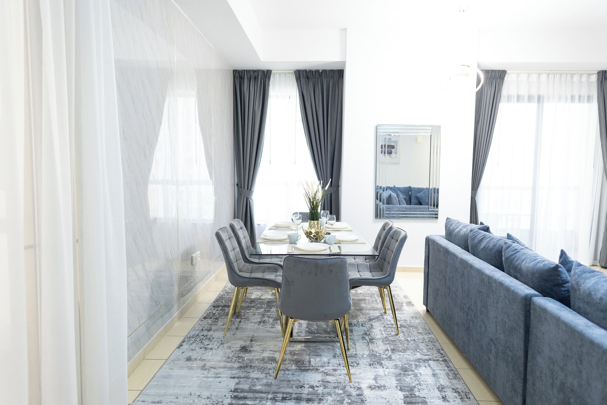 Ein moderner Essbereich mit einem Glastisch, grau gepolsterten Stühlen und einem grauen Sofa.