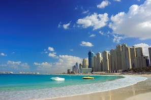 A beachfront cityscape with high-rise buildings, a sandy beach, and boats in the water.