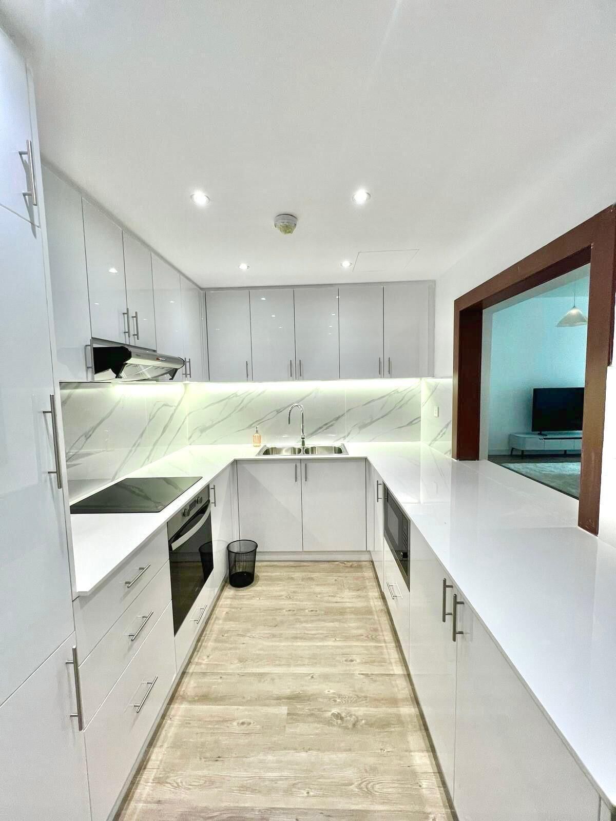 A modern kitchen with white cabinetry, a marble backsplash, and a wooden floor.