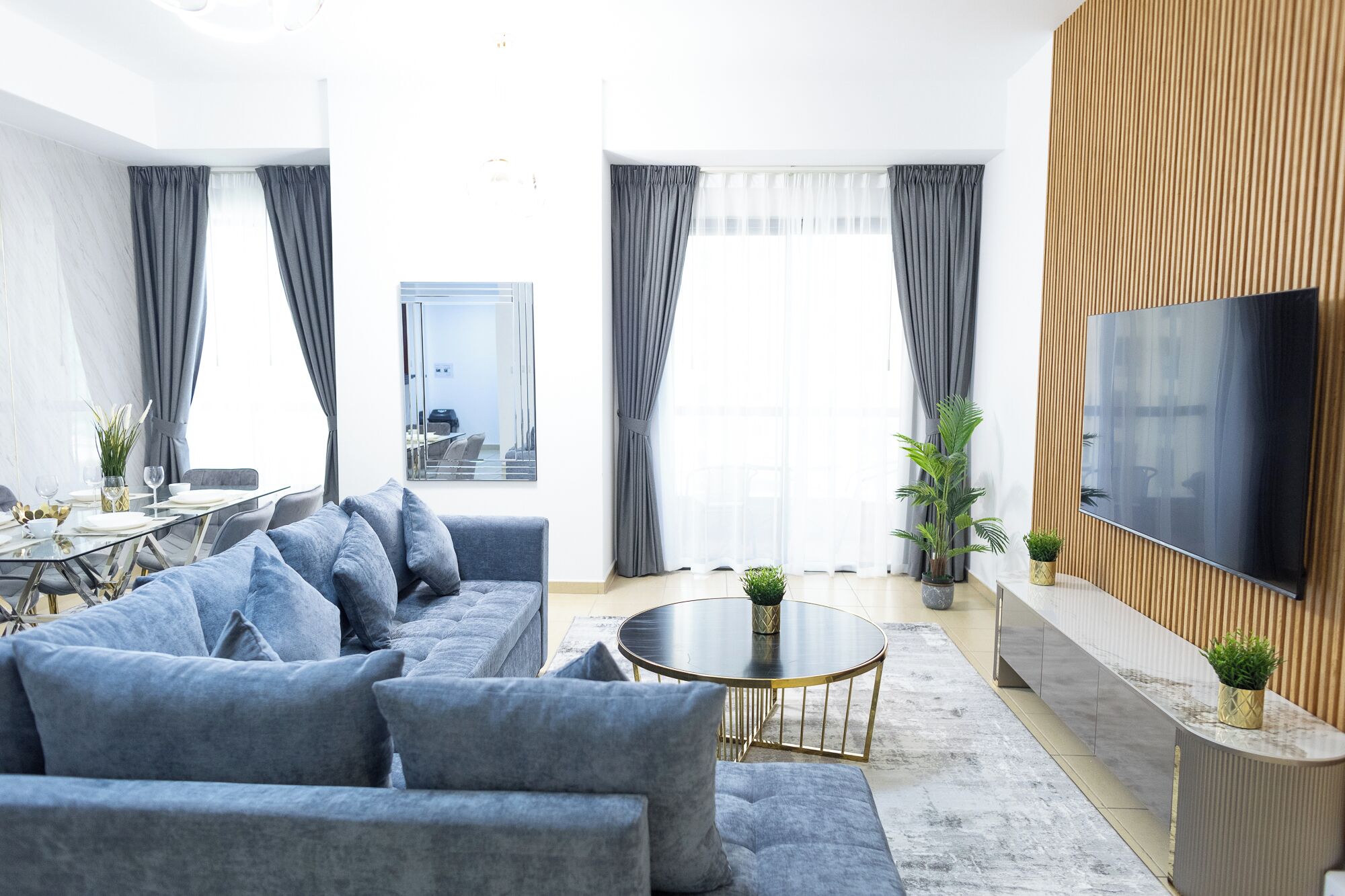 A modern living room with a grey sofa, a round coffee table, and a flat-screen TV mounted on a wooden panel wall.