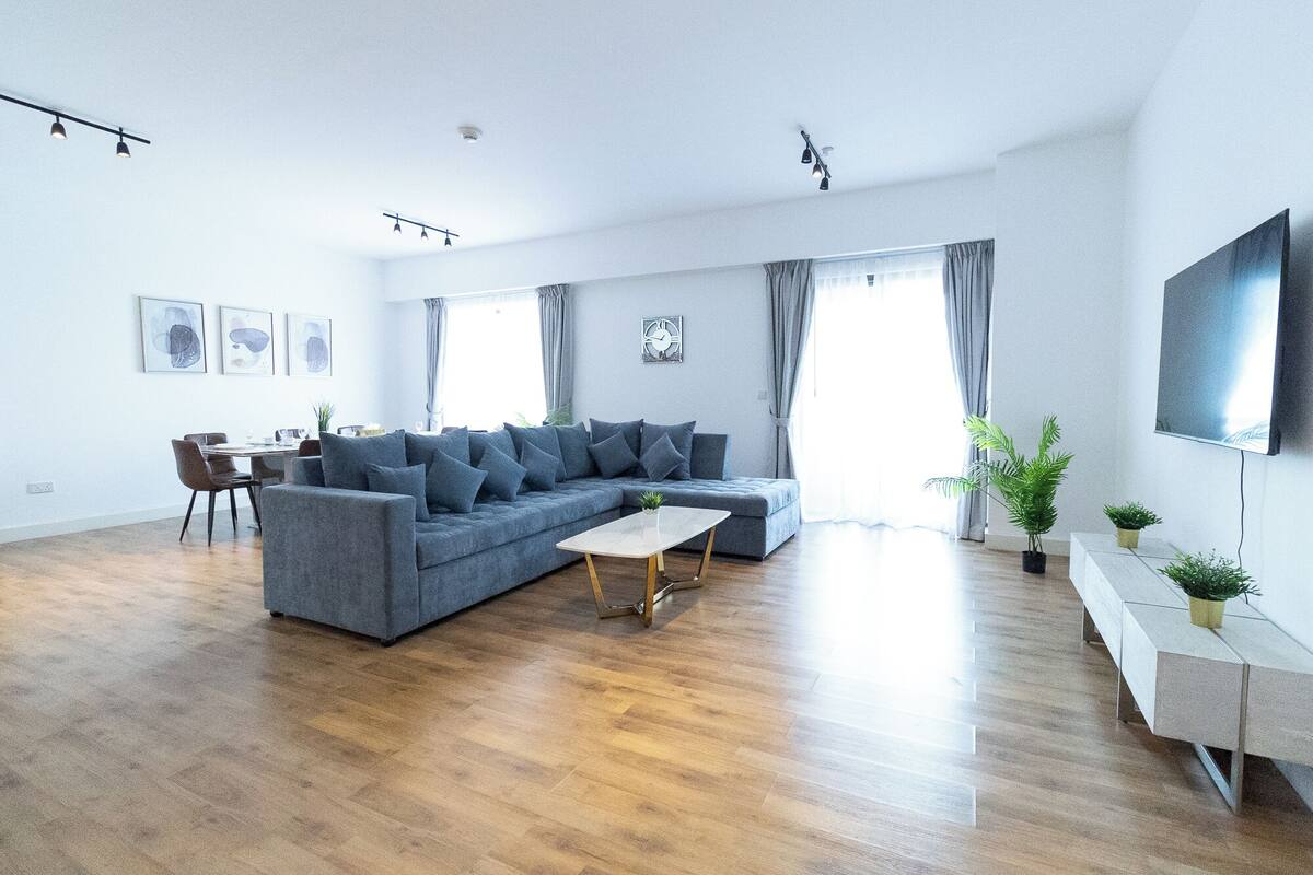 A modern living room with a grey sectional sofa, a coffee table, and a flat-screen TV mounted on the wall.