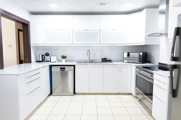 A modern kitchen with white cabinetry, a dishwasher, a sink, a microwave, and a stove. - HAPPY SEASON | JBR Apartments  (Dubai)