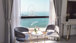 A room with two chairs and a small table, a potted plant, and a view of a large Ferris wheel and water body. - HAPPY SEASON | JBR Apartments  (Dubai)