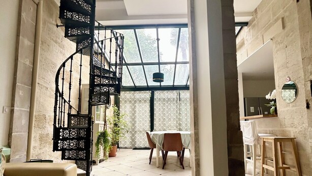 Un vaste espace de vie doté d’une table en verre, d’un escalier en colimaçon et offrant une vue sur l’extérieur.