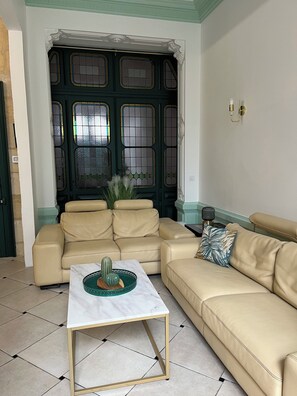 Un salon avec un canapé beige, une table basse blanche et une porte verte ornée de panneaux de verre décoratifs.