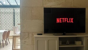 Un salon avec un téléviseur affichant le logo de Netflix, un coin repas avec des chaises et une table, et une piscine à fond de verre.