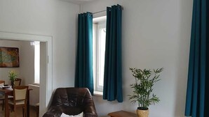 Une chambre à coucher avec un lit, une chaise en bois, une petite armoire, une plante en pot et un ventilateur de plafond.