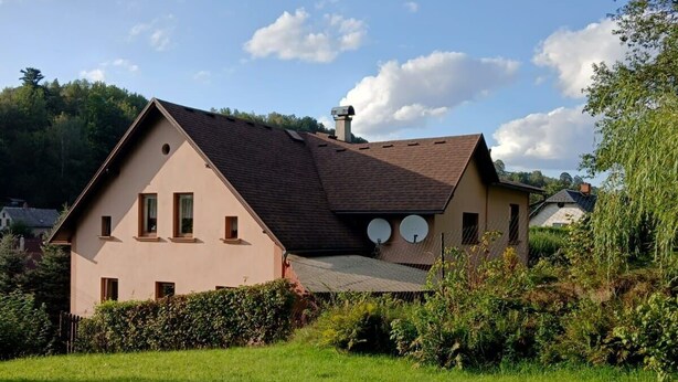 Une maison à deux étages, avec un toit en pente, des antennes paraboliques et une cheminée.