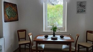 Un coin repas avec une table en bois, six chaises, un luminaire suspendu, une fenêtre avec des stores et une petite plante posée sur le rebord de la fenêtre.