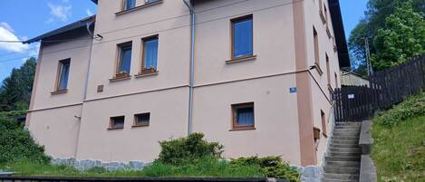Un immeuble à plusieurs étages, avec un mur de pierre à l’avant et une clôture en bois sur le côté droit.