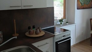 Une cuisine moderne avec des meubles blancs, un évier en acier inoxydable, une cuisinière et une fenêtre donnant sur un paysage verdoyant.