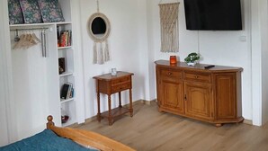 Une chambre à coucher comprenant un lit, une commode en bois, un téléviseur, une petite table, un miroir et une armoire.