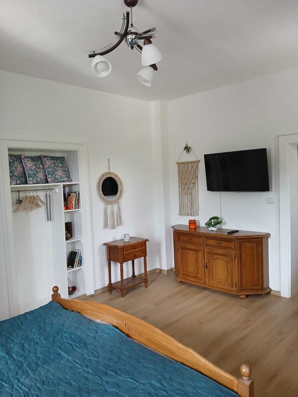 Ein Schlafzimmer mit einem Bett, einer Holzkombination, einem Fernseher, einem kleinen Tisch, einem Spiegel und einem Kleiderschrank.