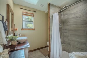 A bathroom with a wooden shower, a sink with a mirror, and a window.
