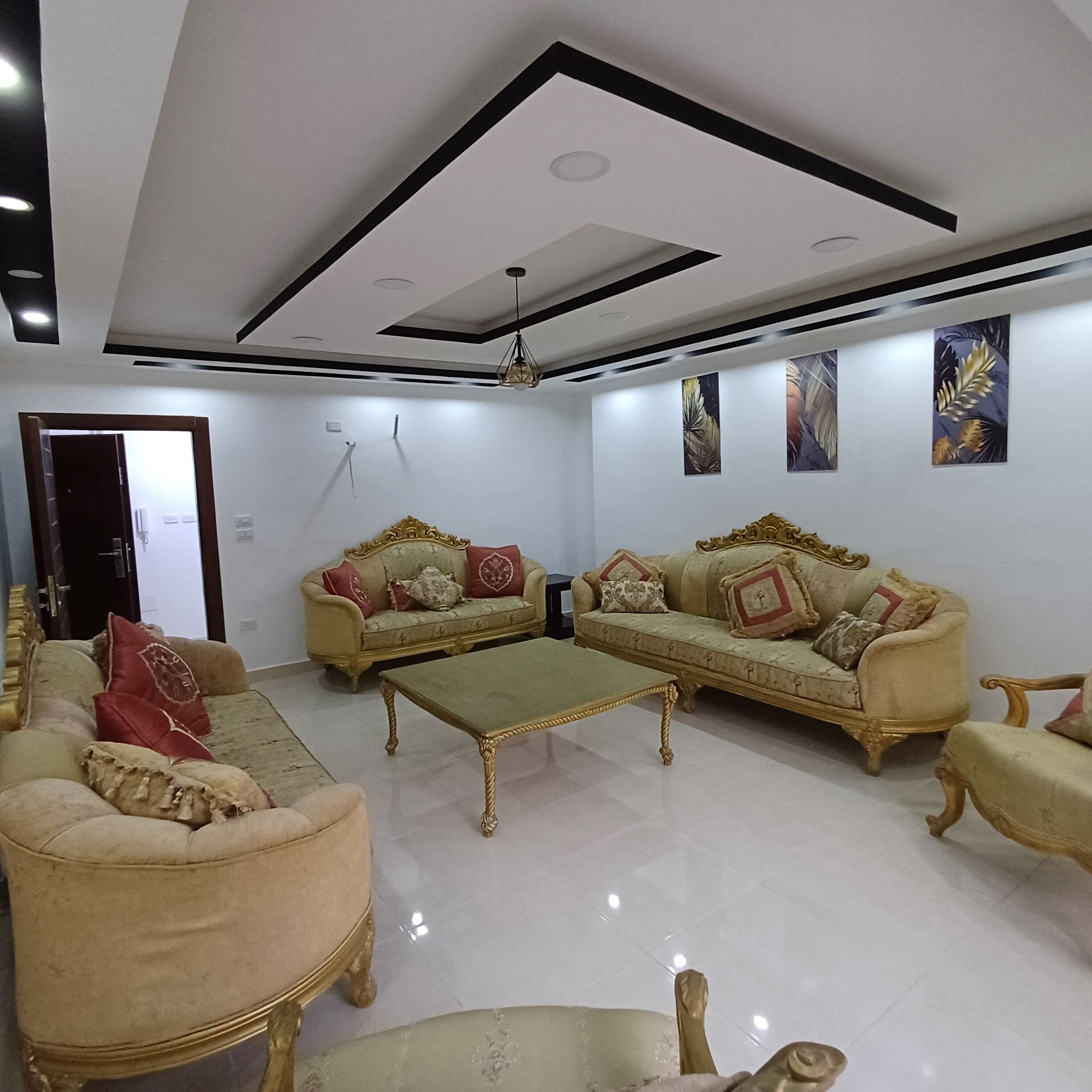 A spacious living room with two sofas, a coffee table, and a chair. The room has a high ceiling with recessed lighting and a modern design.