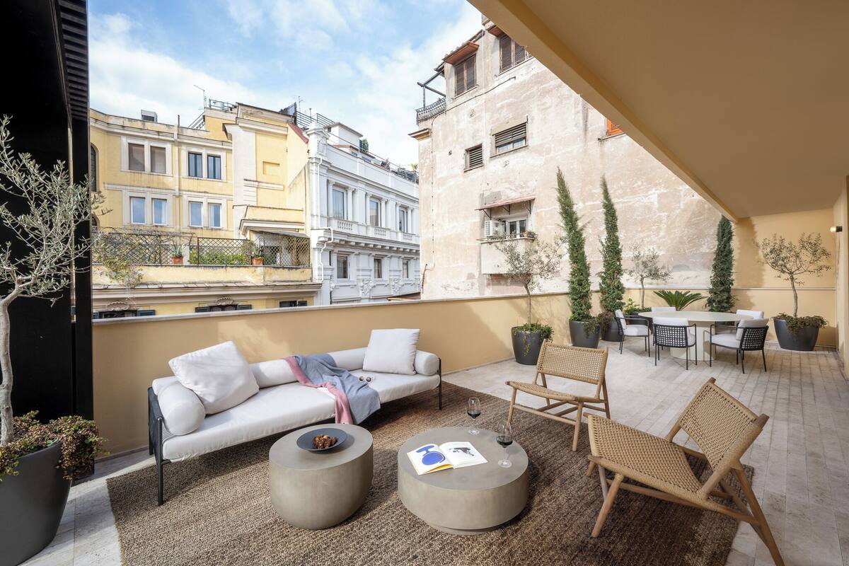 A rooftop terrace with a sofa, round tables, and potted plants.