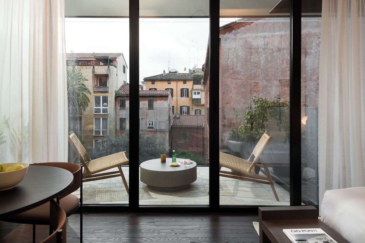 A modern room with a large window, a round table, two wicker chairs, and a bed.