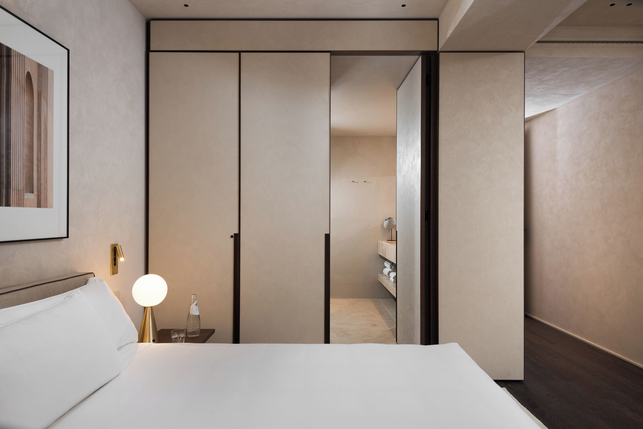 Een moderne hotelkamer met een groot bed, een nachtkastje met een lamp en uitzicht op een badkamer.