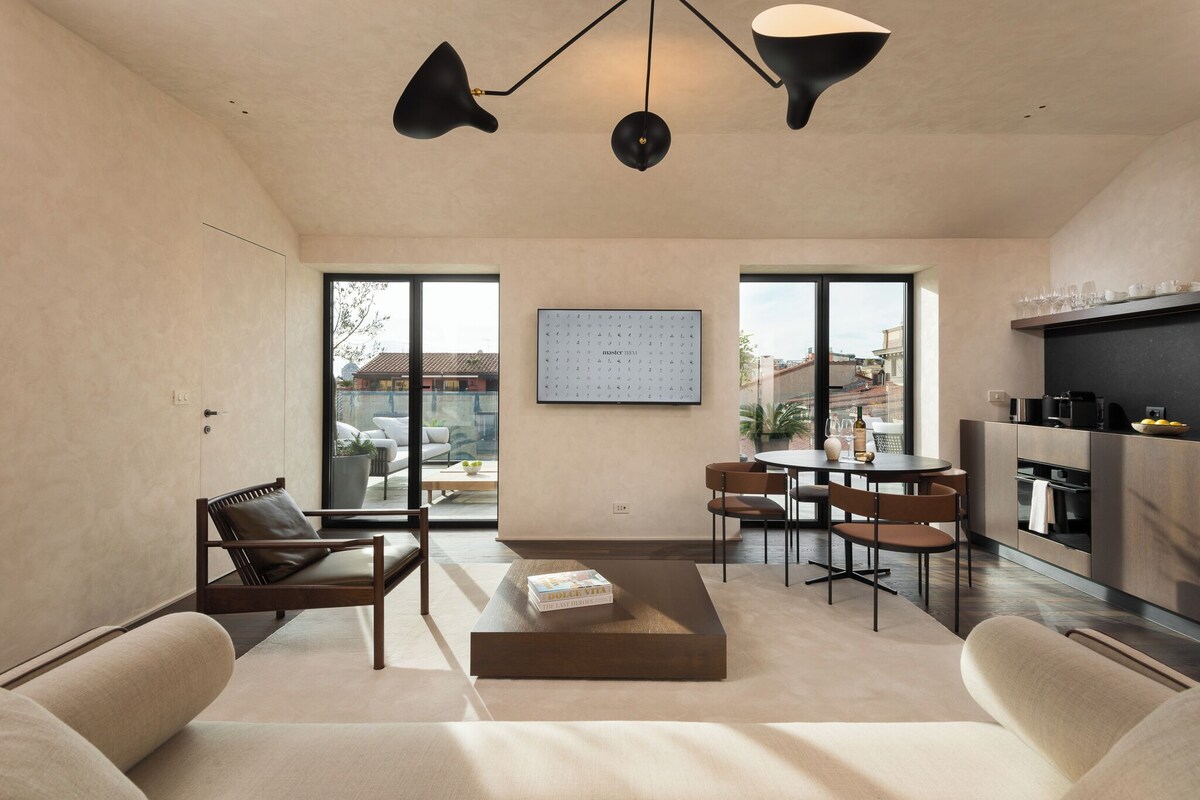 Uma sala de estar moderna com sofá, mesa de centro e área de jantar. Há uma janela grande que oferece vista para o exterior.