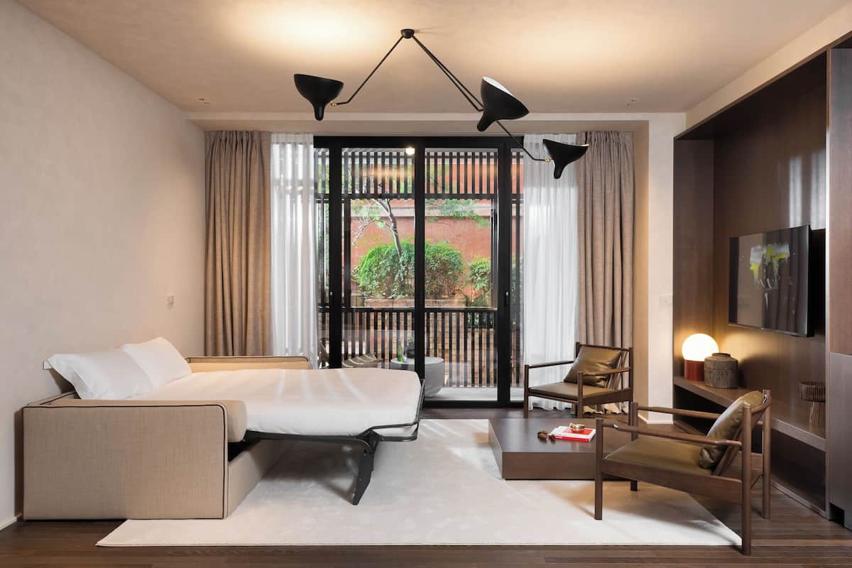 A modern hotel room with a bed, a sofa, a chair, a coffee table, and a TV.