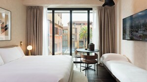 Habitación de hotel con una cama grande, otra más pequeña, una mesa redonda y vistas de edificios a través de la ventana.