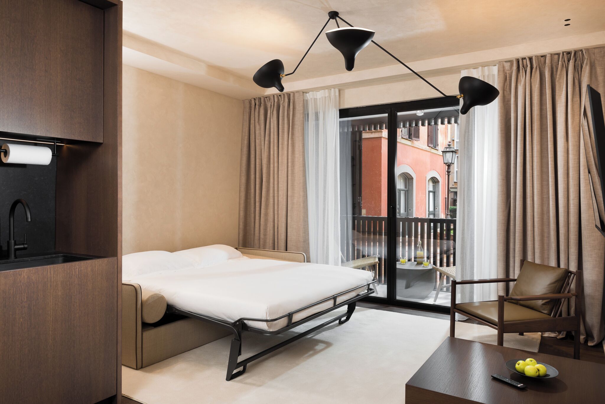 A modern hotel room with a bed, a desk, a chair, and a balcony with a view of the city.