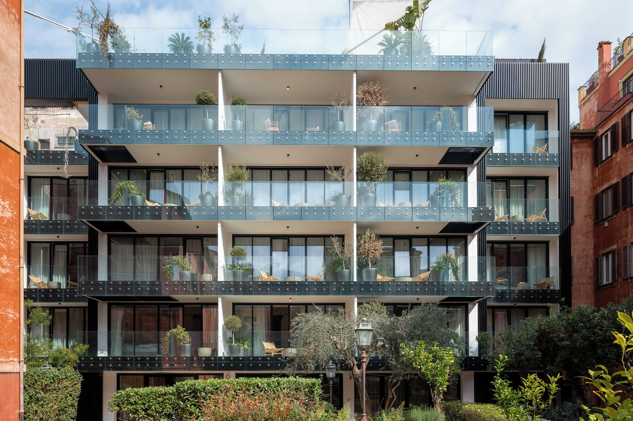 A multi-story building with balconies, large windows, and potted plants.