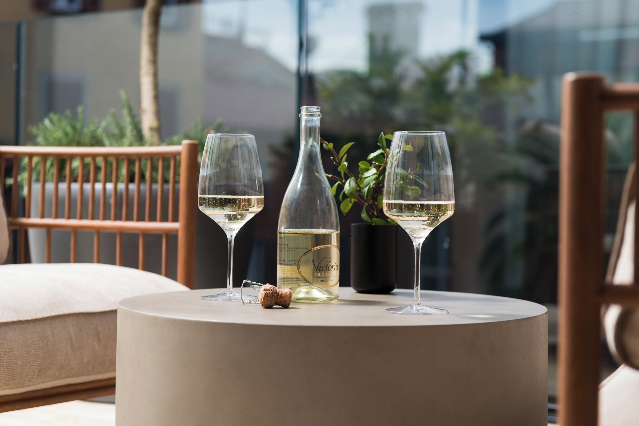 A table with two glasses of white wine, a bottle, and a cork.