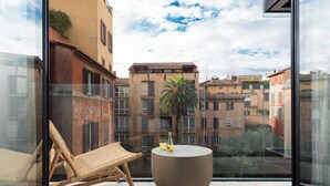 Un balcón con una silla de mimbre, una mesa redonda y una botella de zumo de naranja.