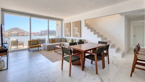Amplia sala de estar con una gran mesa de comedor, asientos cómodos y una escalera que conduce a un piso superior.