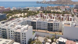 Un moderno complejo de apartamentos con varios edificios, un estacionamiento y vistas al mar y montañas de fondo.