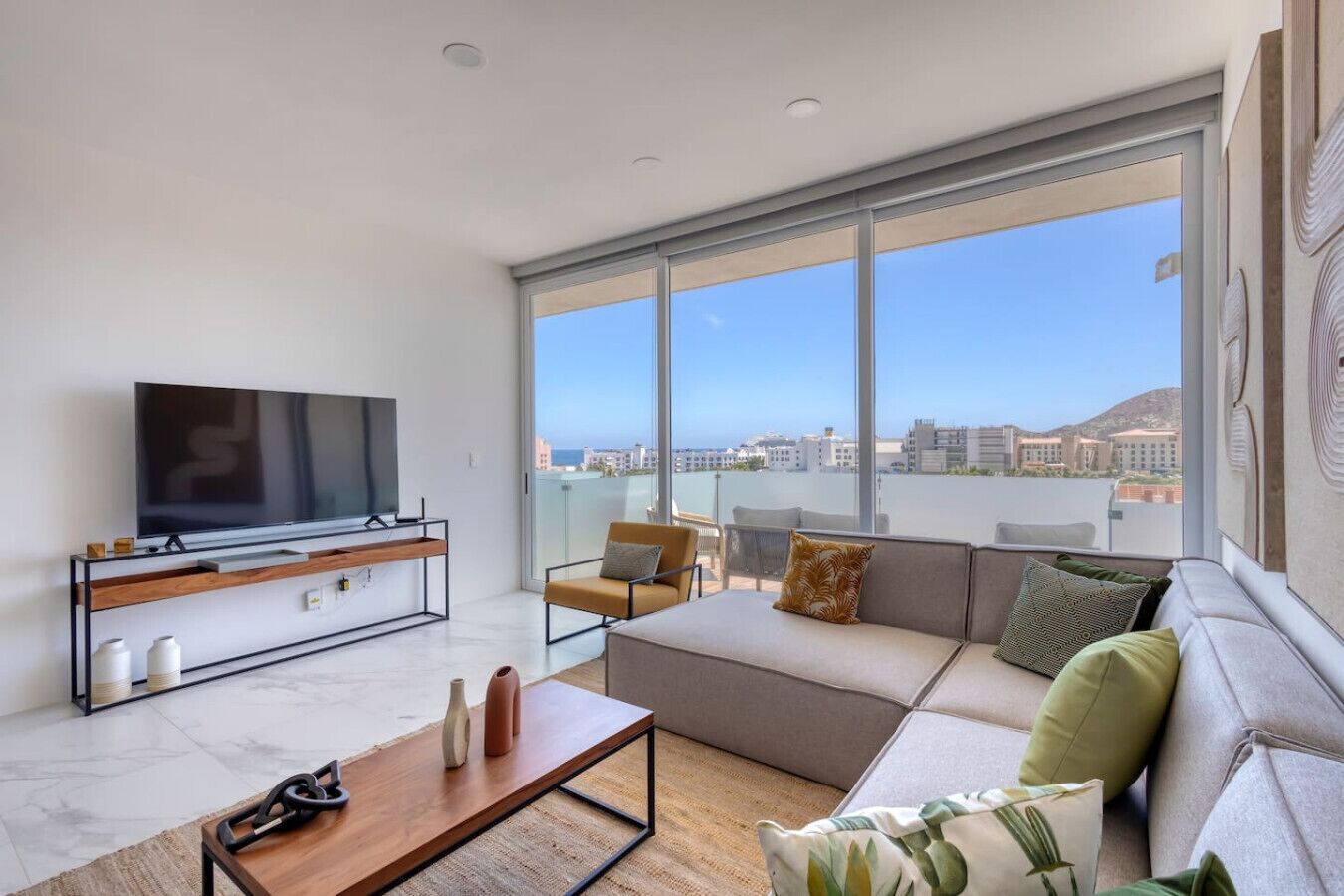 A modern living room with a large TV, a sofa, a coffee table, and a balcony with a city view.