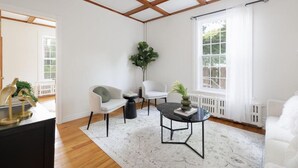 Ein modernes Wohnzimmer mit hohen Decken, weißen Wänden und einem großen Fenster. Es gibt zwei weiße Sessel, einen runden Couchtisch und einen Blumentopf.