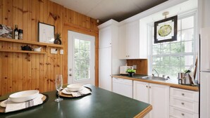 Eine Küche mit Holzwandverkleidung, weißen Schränken, einer grünen Arbeitsplatte und einem Fenster mit Buntglasdekor.