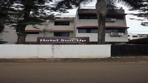 A sign for Hotel Sun-Up by Grace Hospitality International, with a white building in the background and a palm tree in the foreground. - Hotel Sun Up (Nashik)