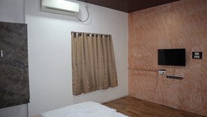A bedroom with a bed, a wall-mounted TV, a curtain, and an air conditioning unit. - Hotel Sun Up (Nashik)