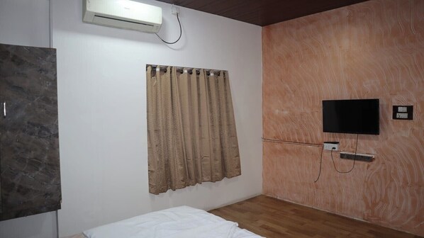 A bedroom with a bed, a wall-mounted TV, a curtain, and an air conditioning unit. - Hotel Sun Up (Nashik)