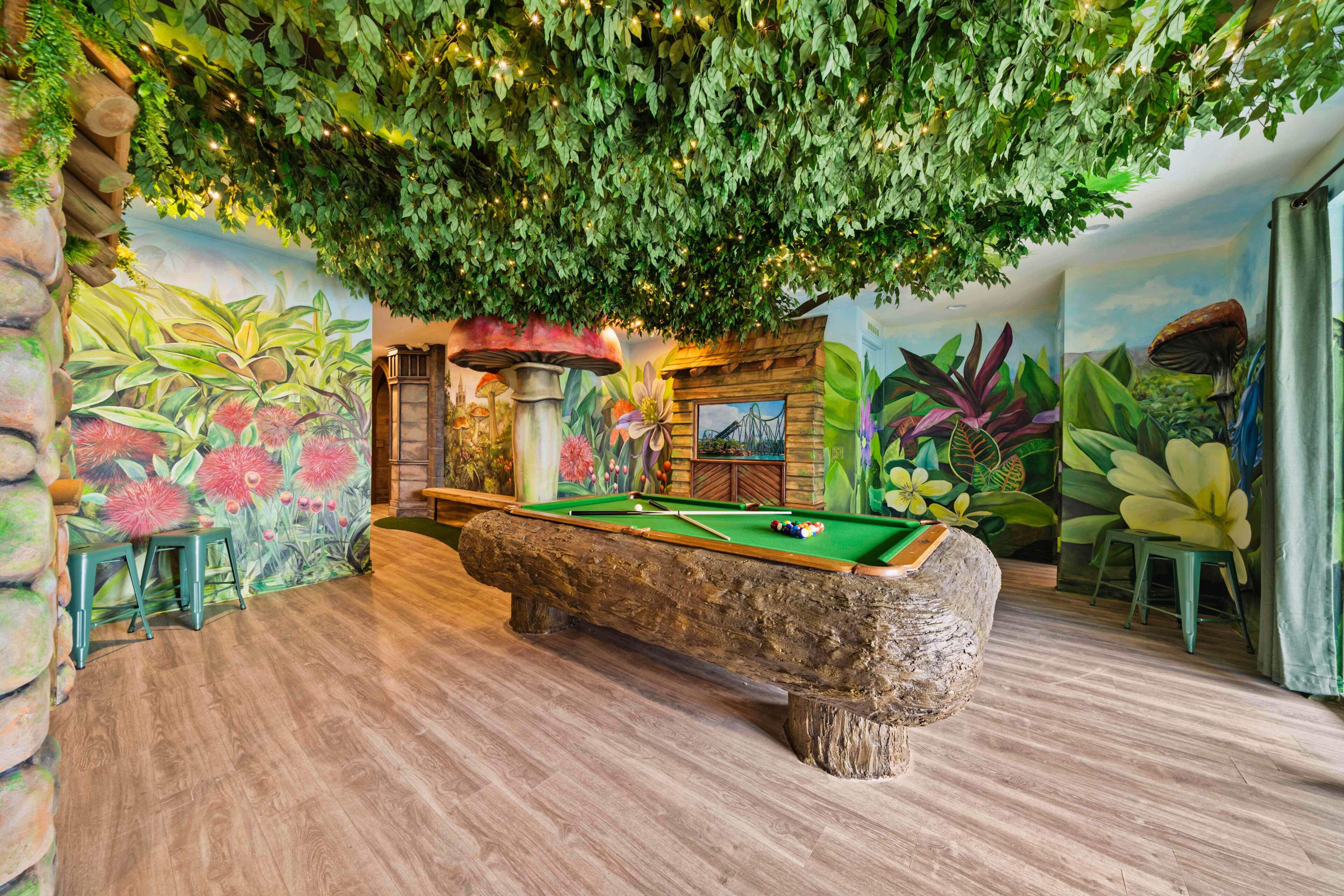 A pool table in a room with a mural of tropical plants and a wooden bench.