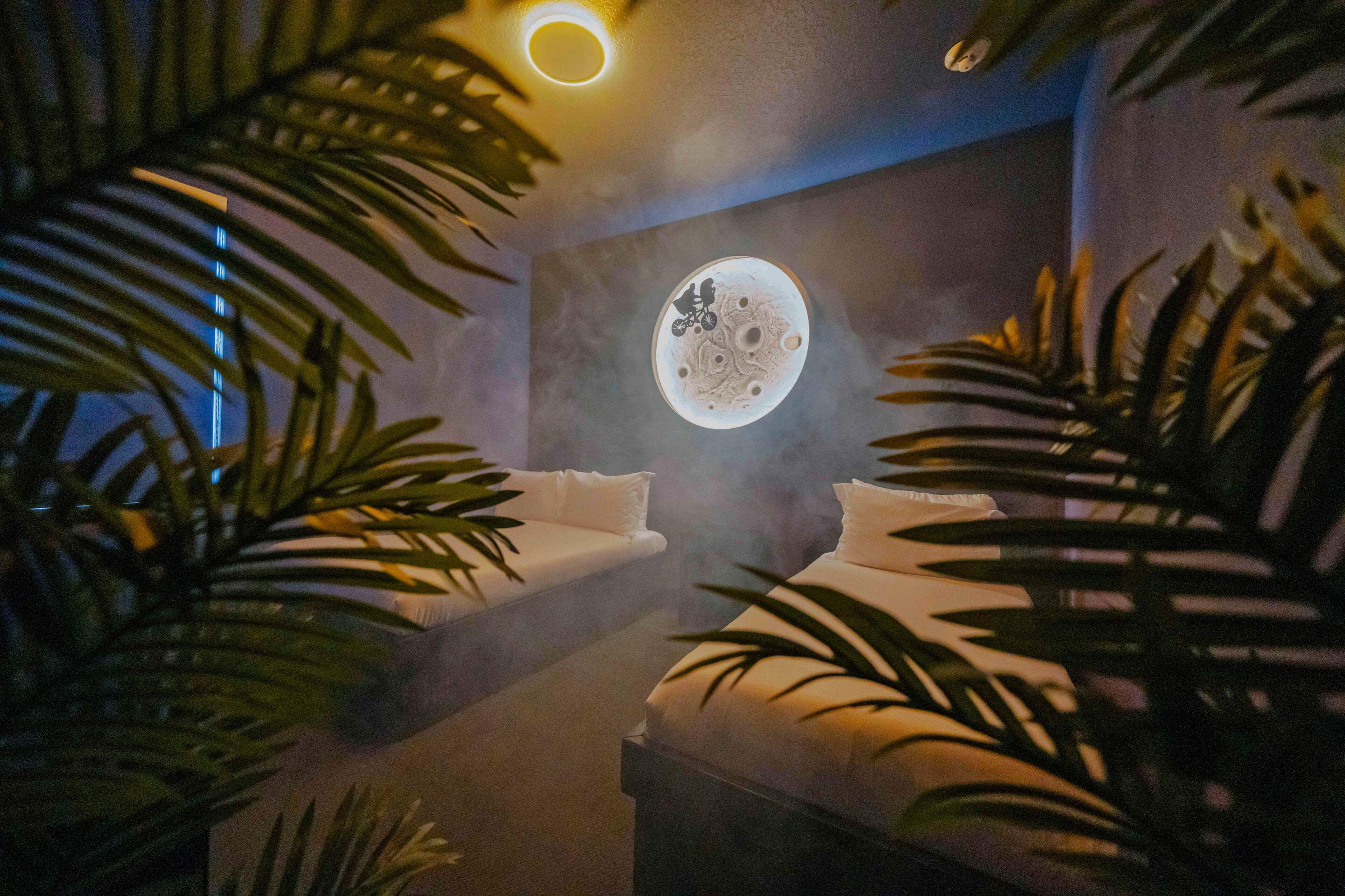 Une salle de spa avec deux lits blancs, un élément décoratif mural circulaire et des plantes tropicales.