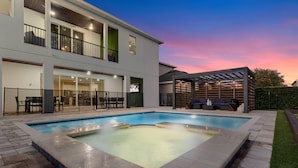 Una casa moderna de dos pisos amb piscina, mobiliari d'exterior i un porxo cobert.