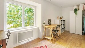A bright room with a large window, a wooden table, a radiator, and a white cabinet. - Charming house with garden near Lyon, airport and Eurexpo (Jonage)