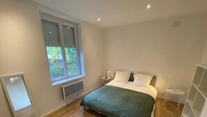 A bedroom with a bed, a window, a radiator, and a bedside table. - Charming house with garden near Lyon, airport and Eurexpo (Jonage)